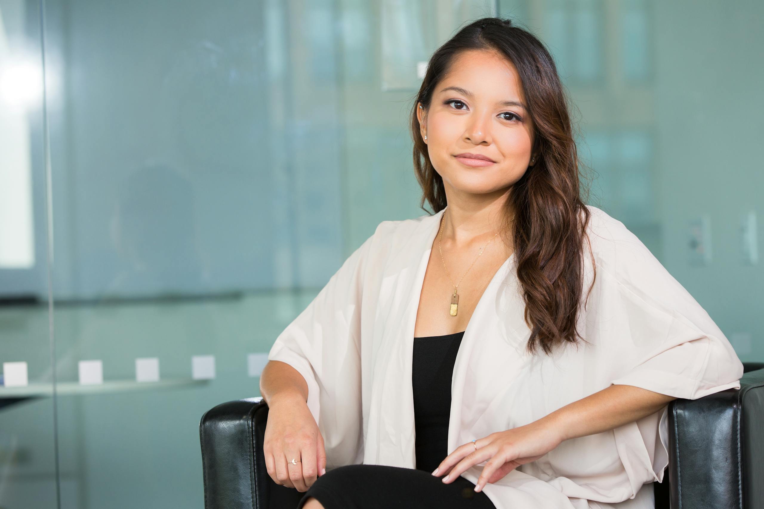 Henkilö A professional Asian businesswoman sitting confidently in a modern office setting.